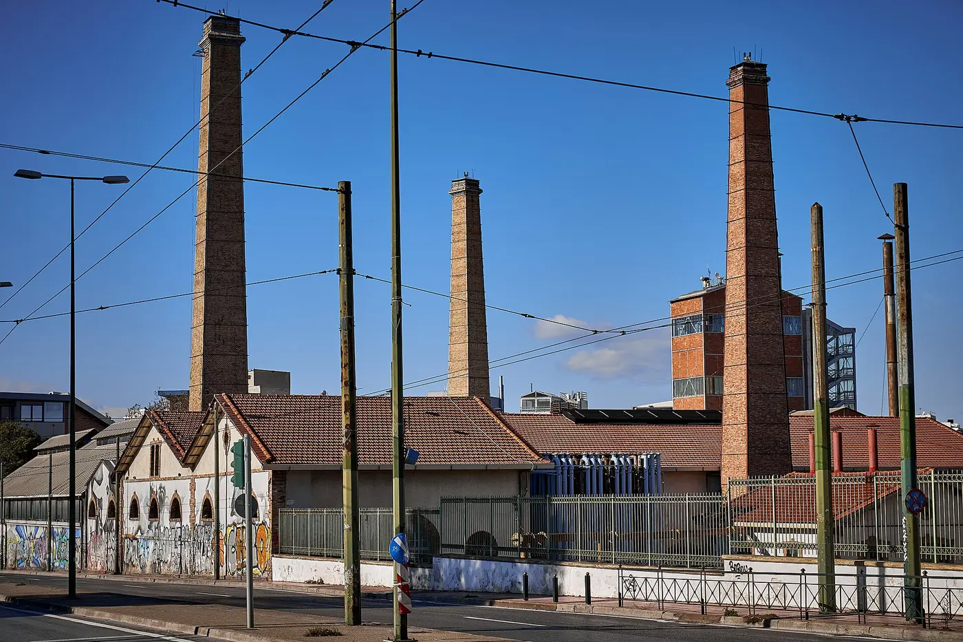 De hoge bakstenen schoorstenen en gebouwen van de oude gasfabriek in Technopolis, onder een helderblauwe lucht