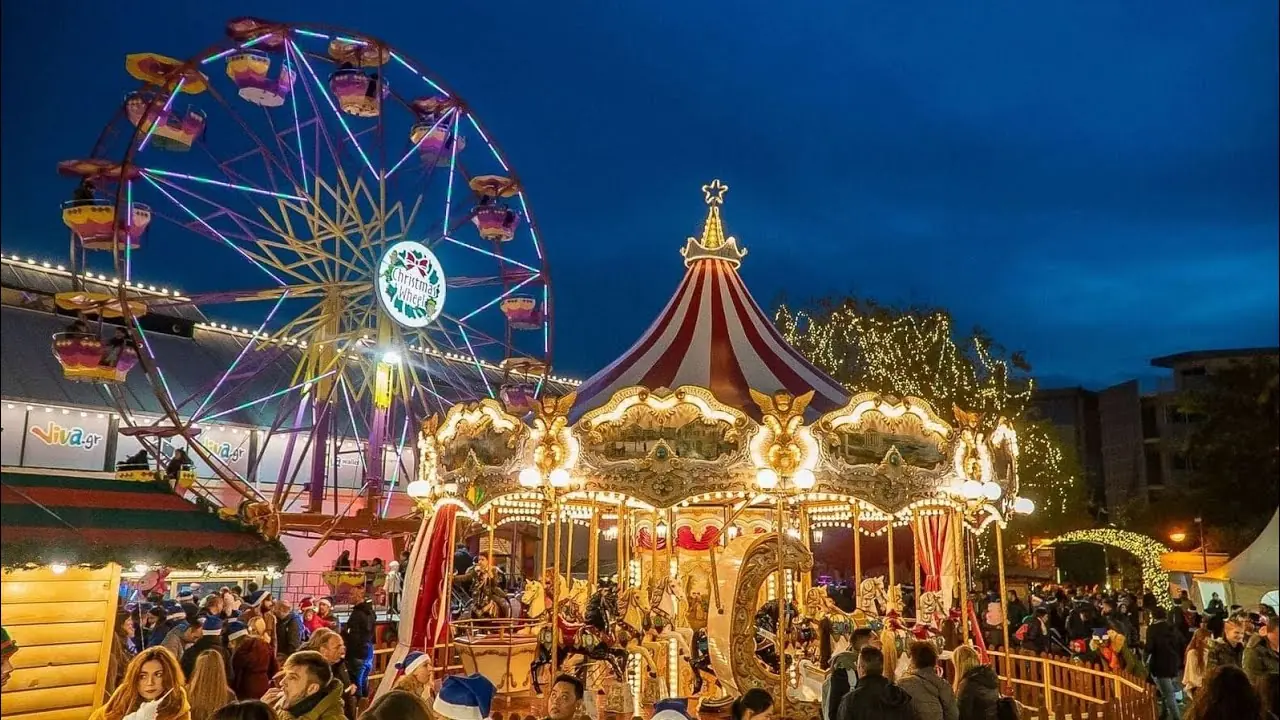 Groot verlicht reuzenrad en draaimolen met rood-wit dak in het kerstdorp van Technopolis in de schemering, met mensen ervoor