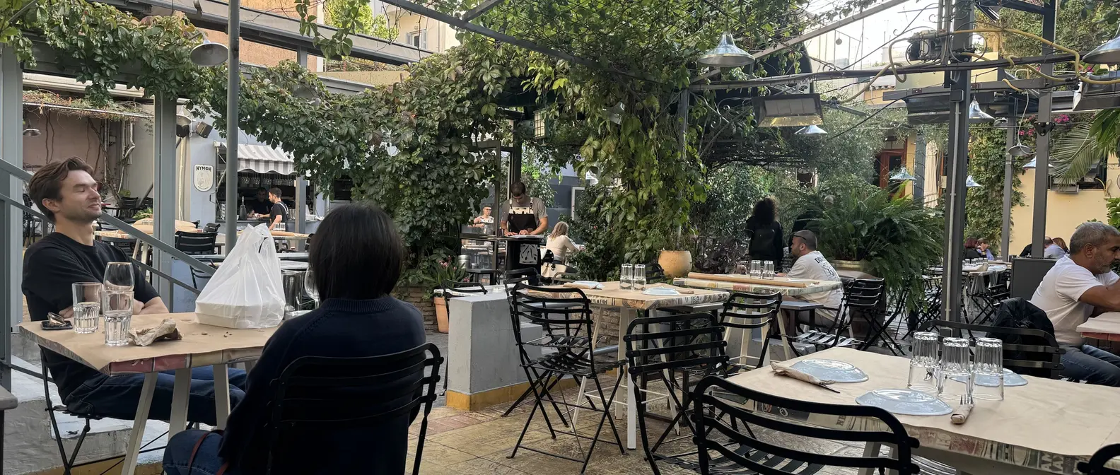 Η αυλή του Άμα Λάχει στα Εξάρχεια με κληματαριές, θερμαντικά και τραπέζια με χάρτινα τραπεζομάντιλα