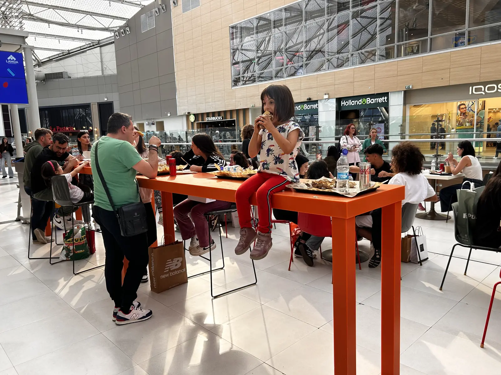 Food court w The Mall Athens na Poziomie 3, ze wspólnymi stolikami i szyldami restauracji