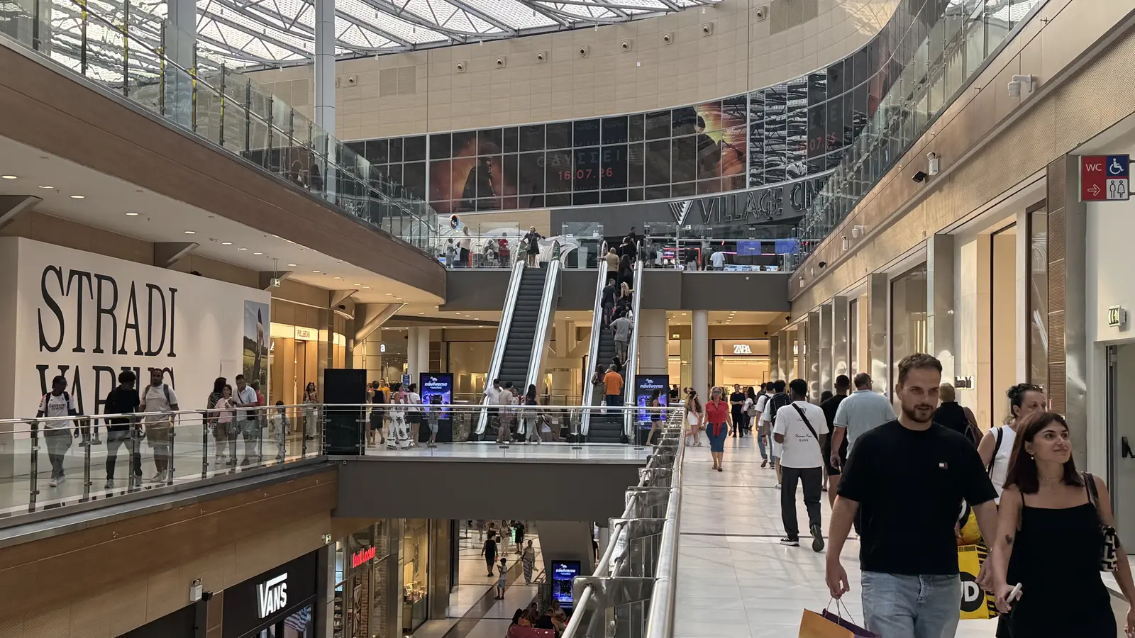 Wnętrze The Mall Athens: jasne korytarze z witrynami sklepowymi i odwiedzającymi na wyższych poziomach