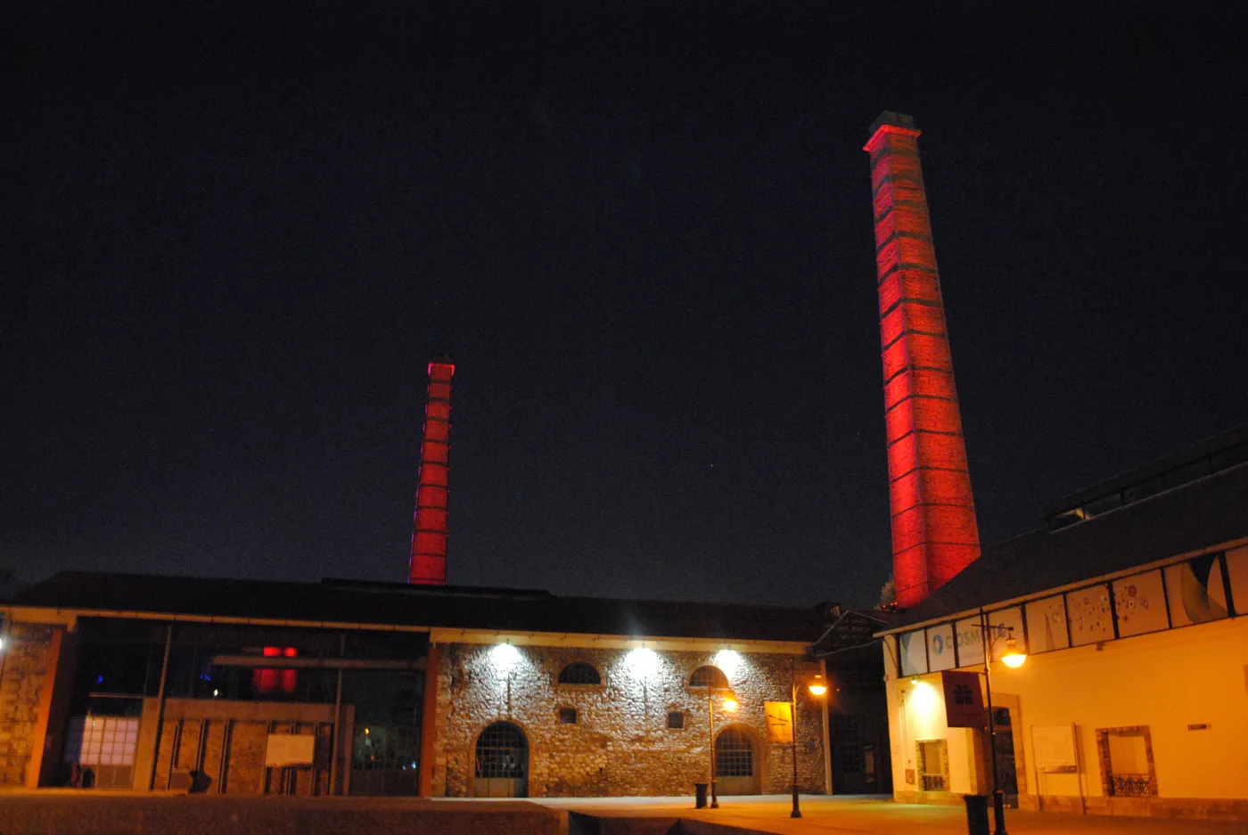 夜里被红光照亮的 Technopolis 烟囱，立在石头建筑上方