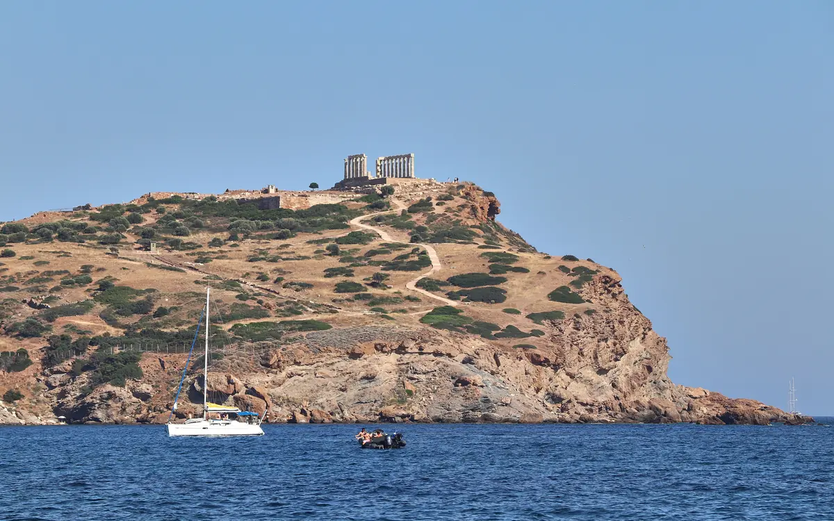 The Temple of Poseidon at Cape Sounio above the sea, with a sailing boat in the background