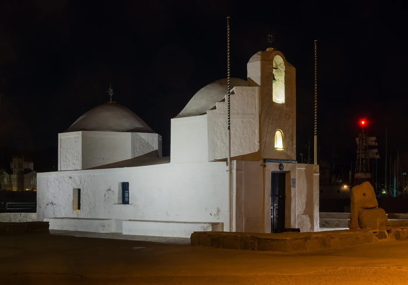 A capela branca de Agios Nikolaos no fim do porto, iluminada à noite