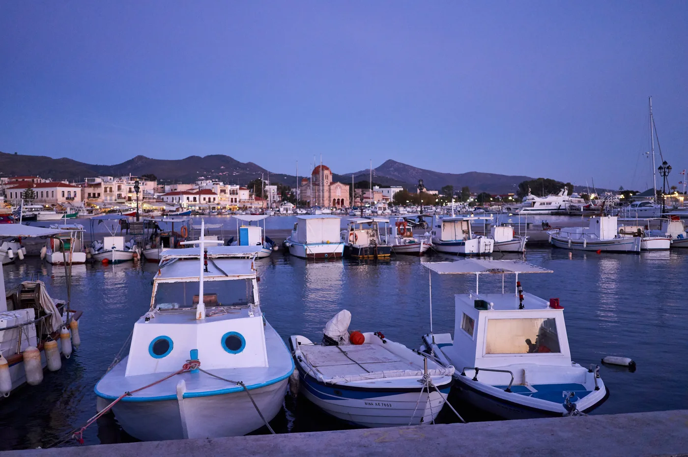 Barcos no porto de Egina ao anoitecer, com a cidade atrás
