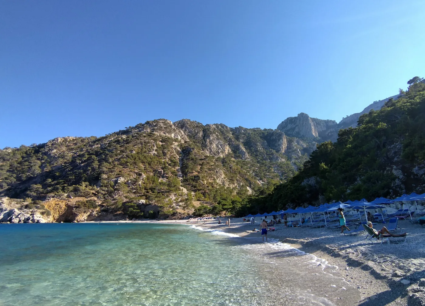 La plage d’Apella avec des galets, une eau claire et des montagnes autour
