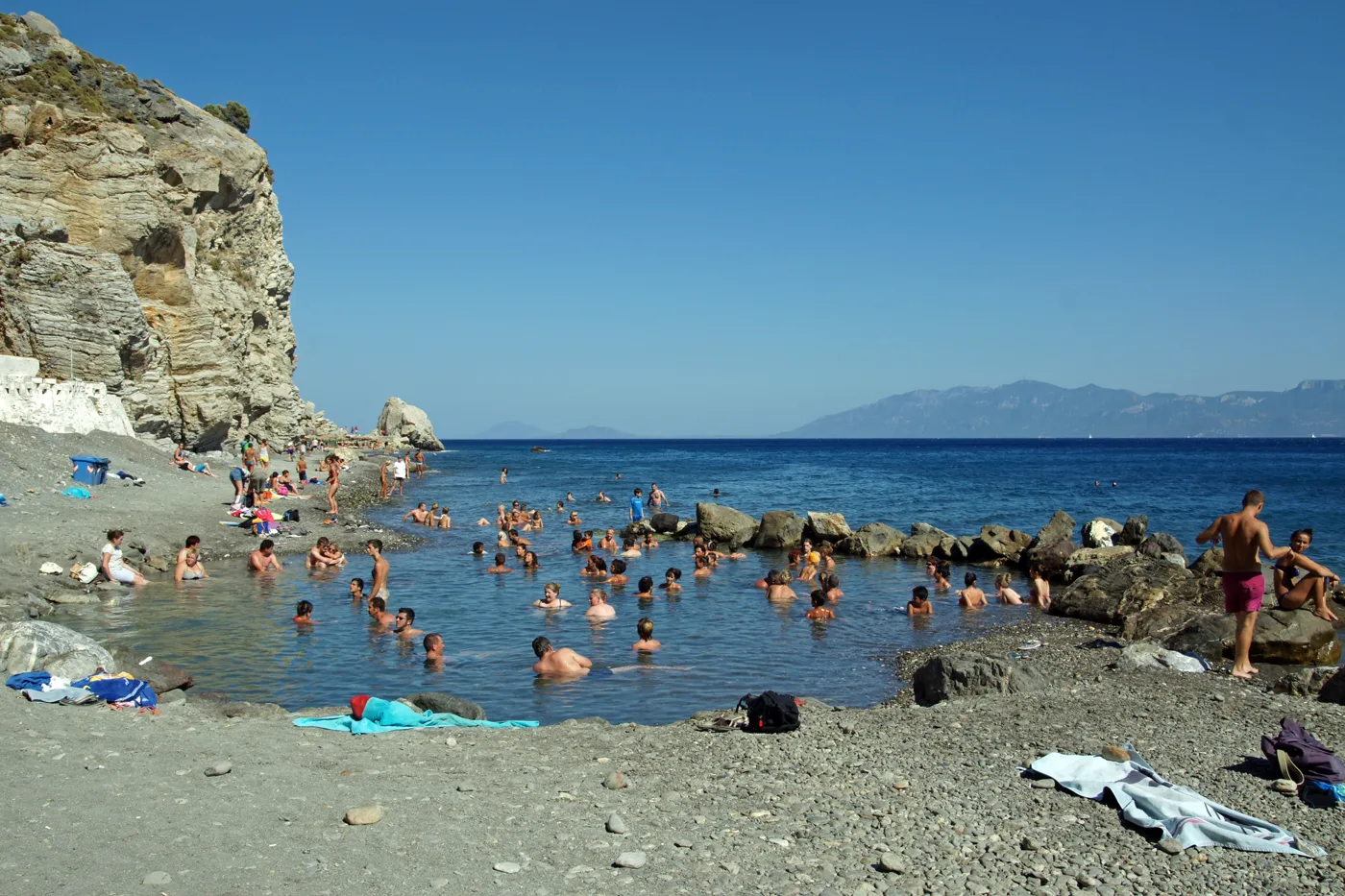 Persone nelle sorgenti calde che scendono in mare, sotto rocce grigie
