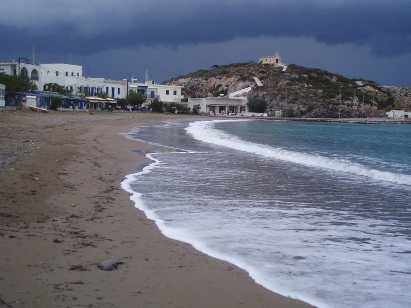 La plage de Kapsali avec des vagues, les maisons et la colline derrière