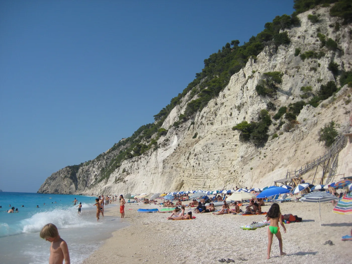La plage d’Egremni avec du monde, des parasols et des vagues sous une falaise blanche