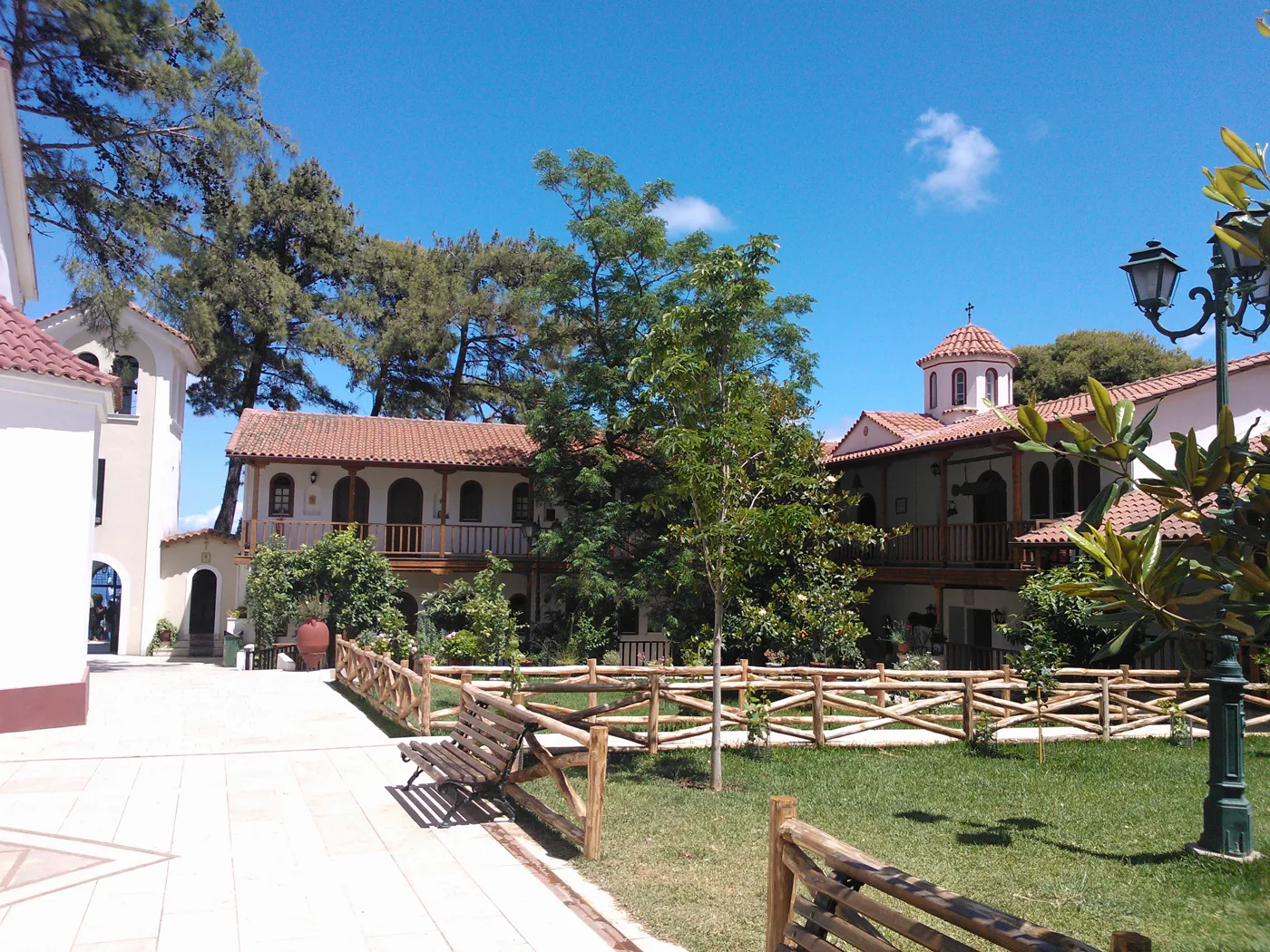 La cour du monastère de Faneromeni avec des arbres, des lanternes et la coupole de l’église
