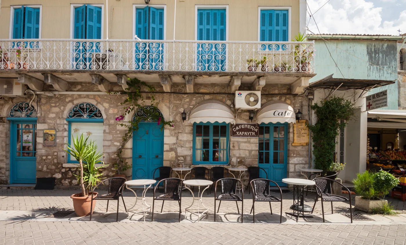 Un vieux bâtiment aux volets bleus, avec des balcons en fer et un café, dans une rue piétonne de Lefkada