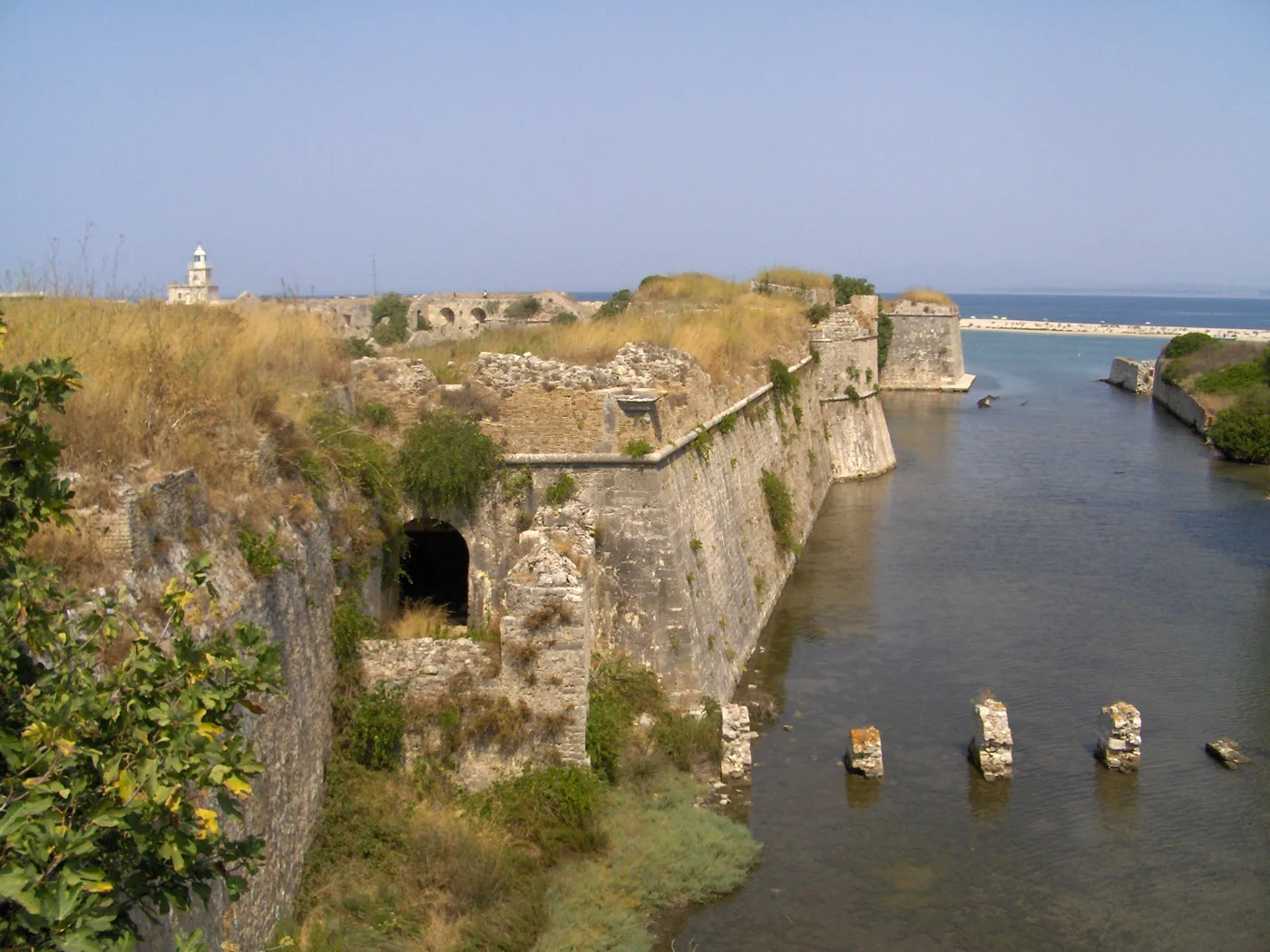 Les murailles du château de Santa Maura au bord du canal, avec le phare au loin
