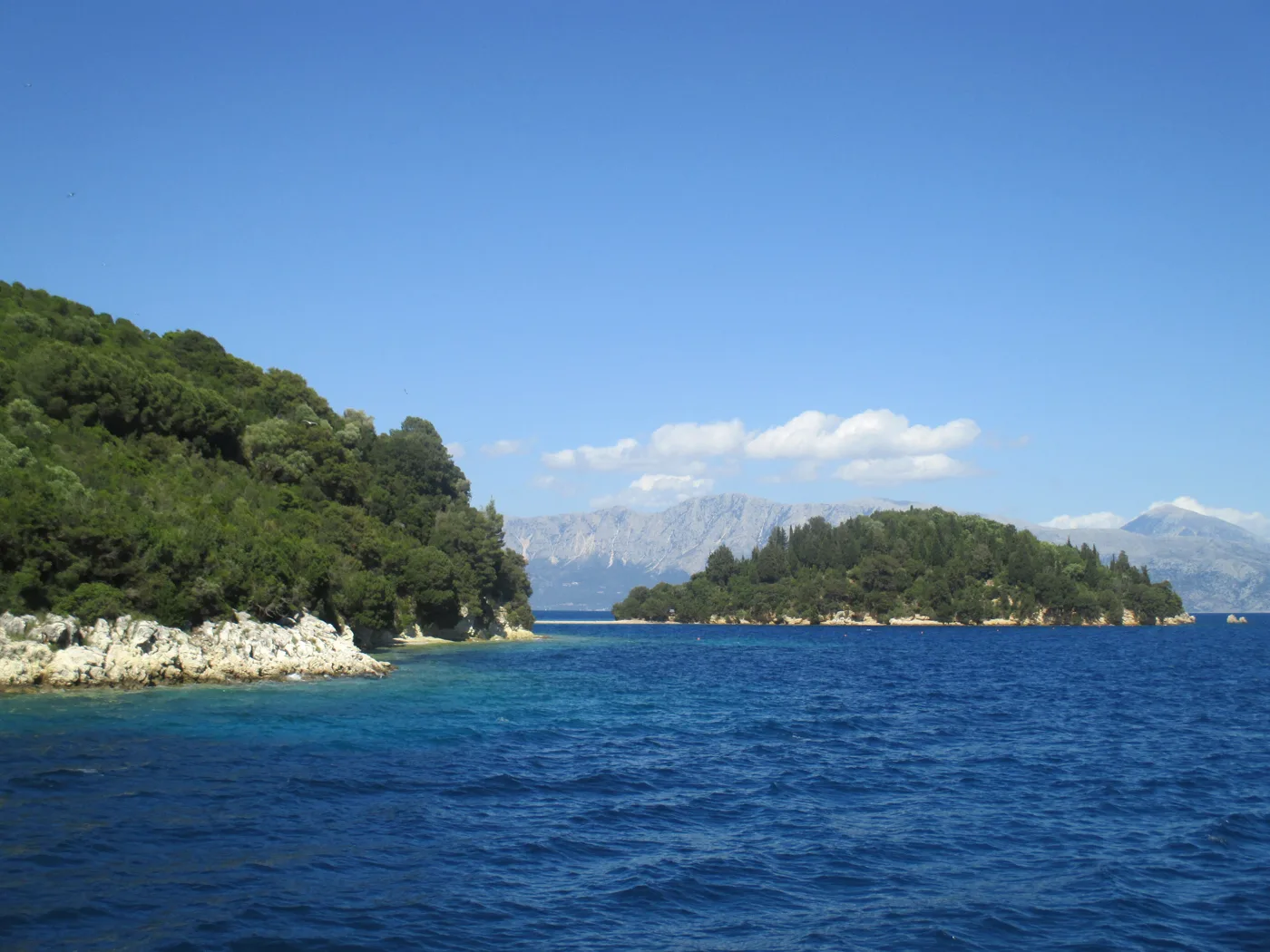 Des îlots verts dans une mer bleue, avec des montagnes au loin, près de Skorpios