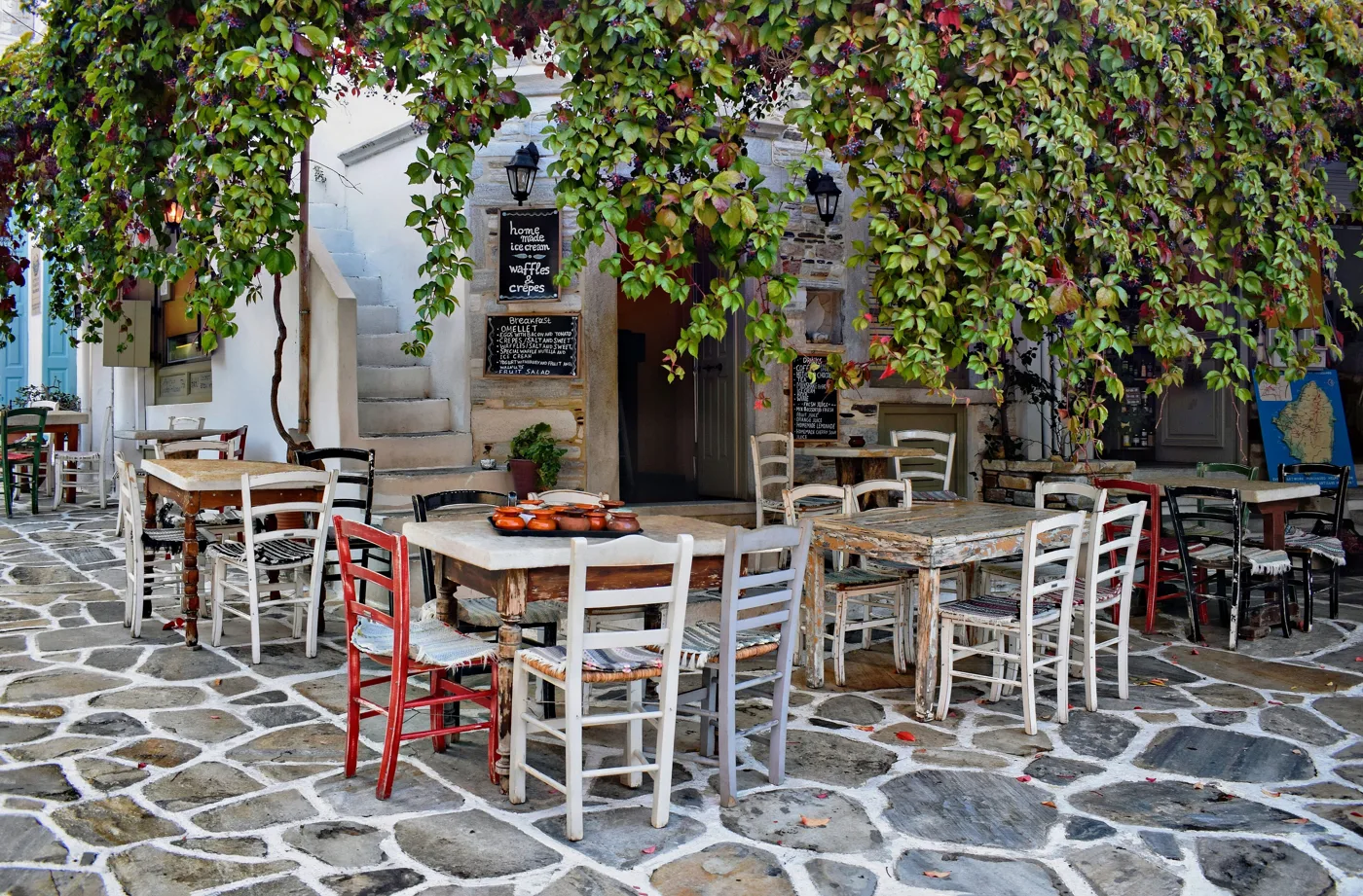 Πλακόστρωτη πλατεία στο Χαλκί με τραπεζάκια ταβέρνας κάτω από κληματαριά