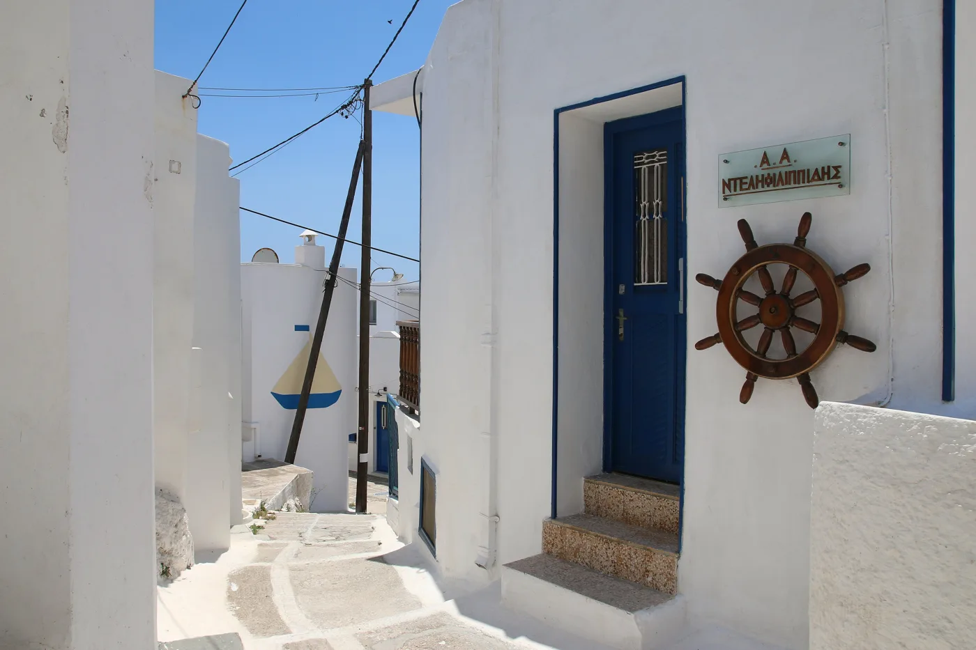 Ένα λευκό σοκάκι της Κάτω Χώρας με γαλάζια πόρτα και ένα τιμόνι καραβιού
