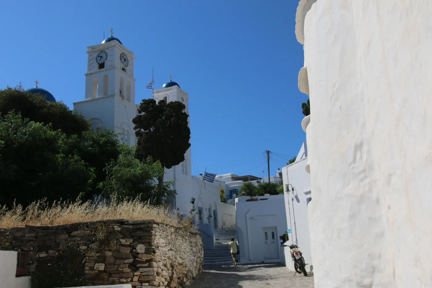 Eine gepflasterte Gasse in Apollonia, mit einem weißen Glockenturm und Bäumen