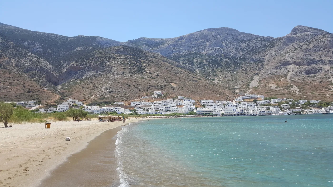 Der Sandstrand von Kamares mit flachem blauem Wasser und Bergen dahinter