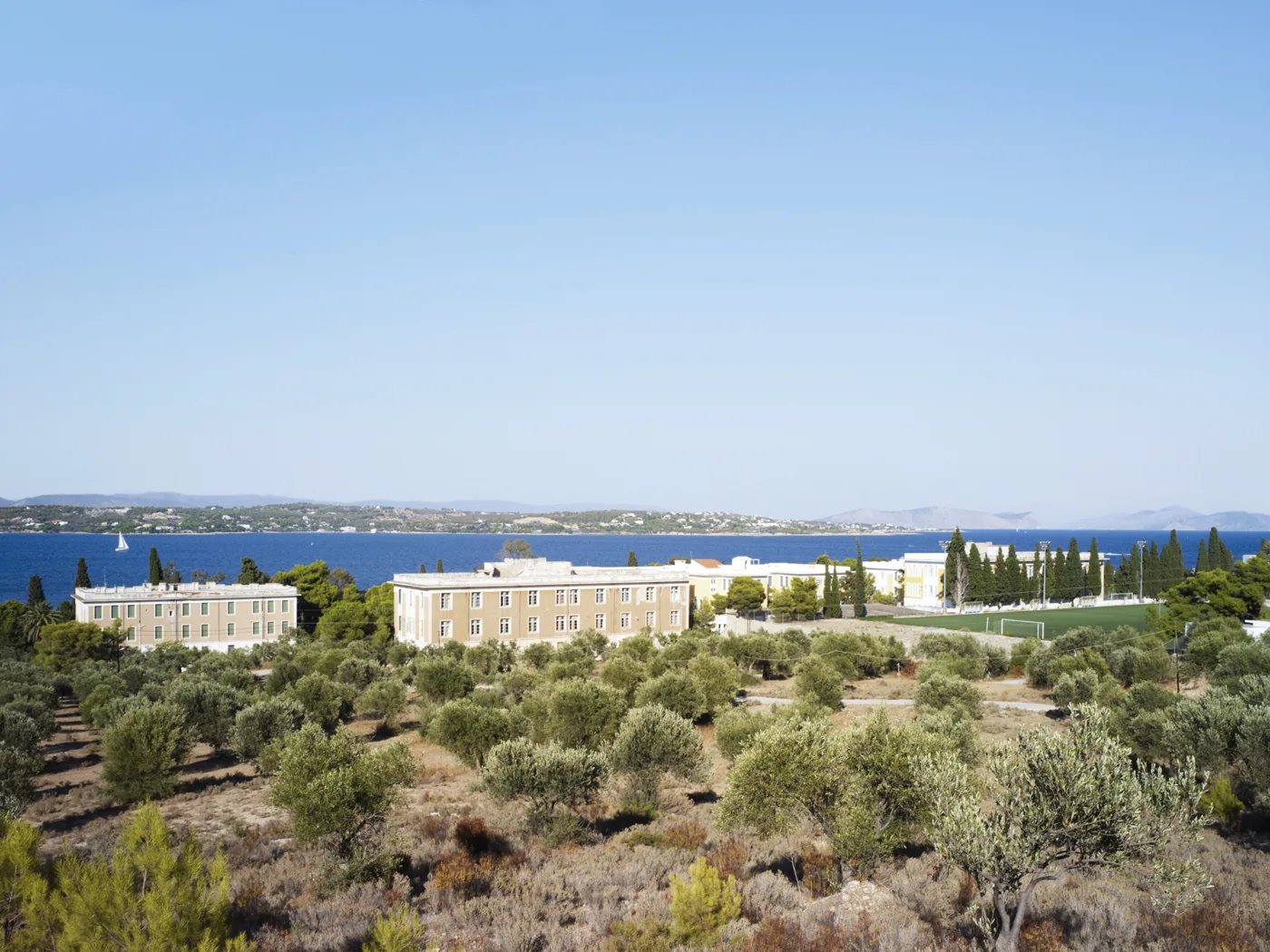 Το μεγάλο κτίριο της Αναργυρείου Σχολής μέσα σε ελιές, με τη θάλασσα πίσω