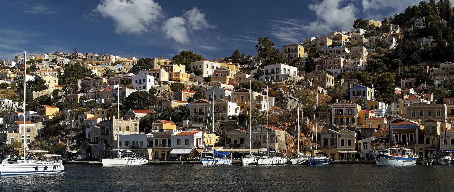 Gialos a Symi con case neoclassiche colorate sul pendio e barche a vela nel porto