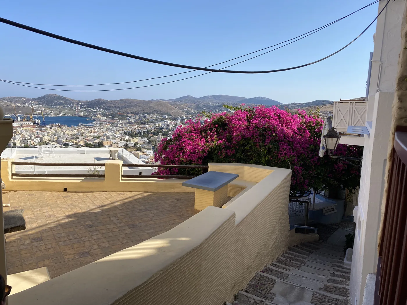 Une terrasse à Ano Syros avec des bougainvilliers et une vue sur Ermoupoli et le port