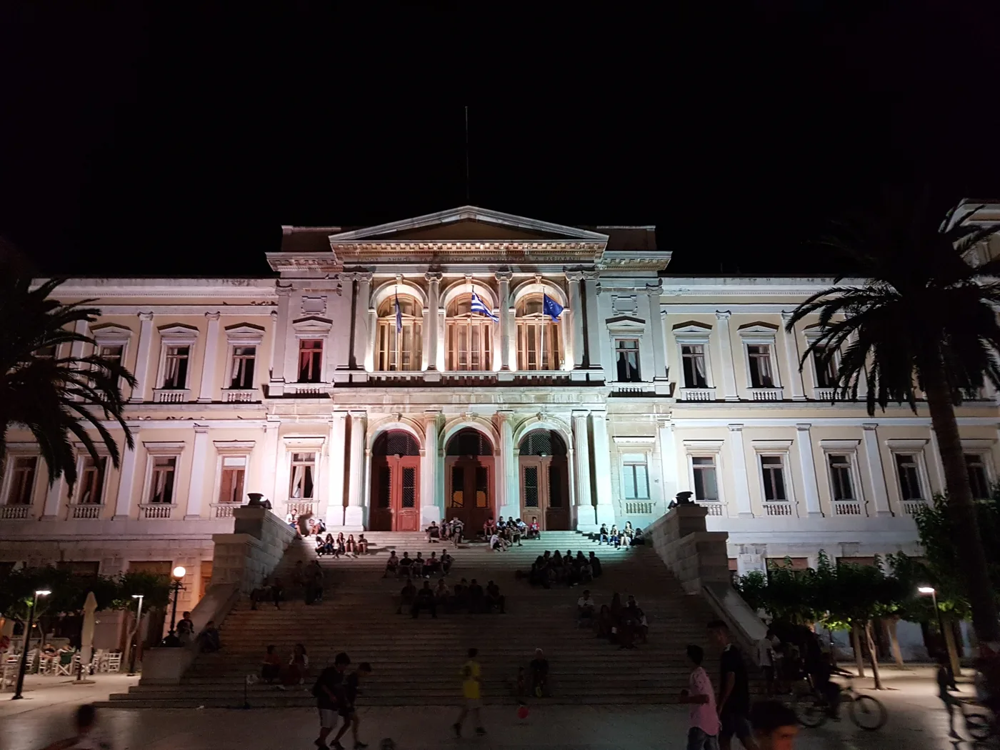 L’hôtel de ville d’Ermoupoli illuminé la nuit, avec du monde sur les marches