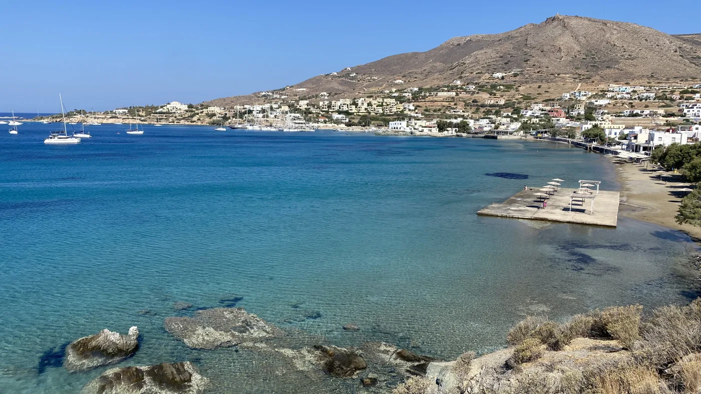La plage de Finikas avec des rochers, des transats et des maisons sur la colline