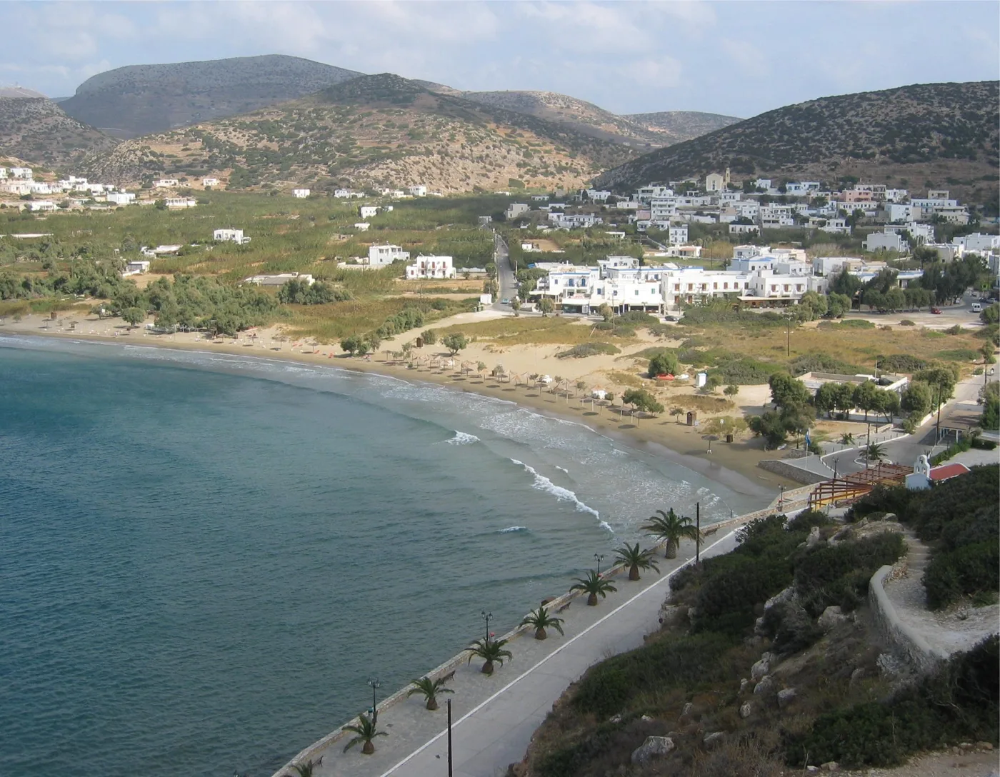 La baie de Galissas avec une longue plage de sable, des maisons et des montagnes derrière