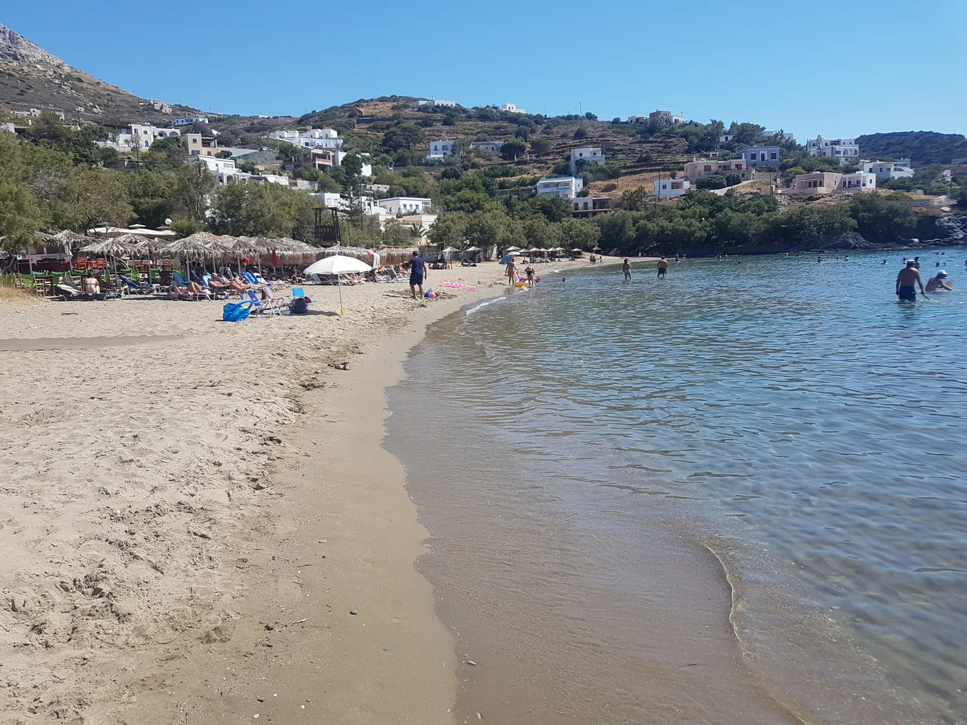 La plage de sable de Kini avec des tavernes et des maisons sur la colline