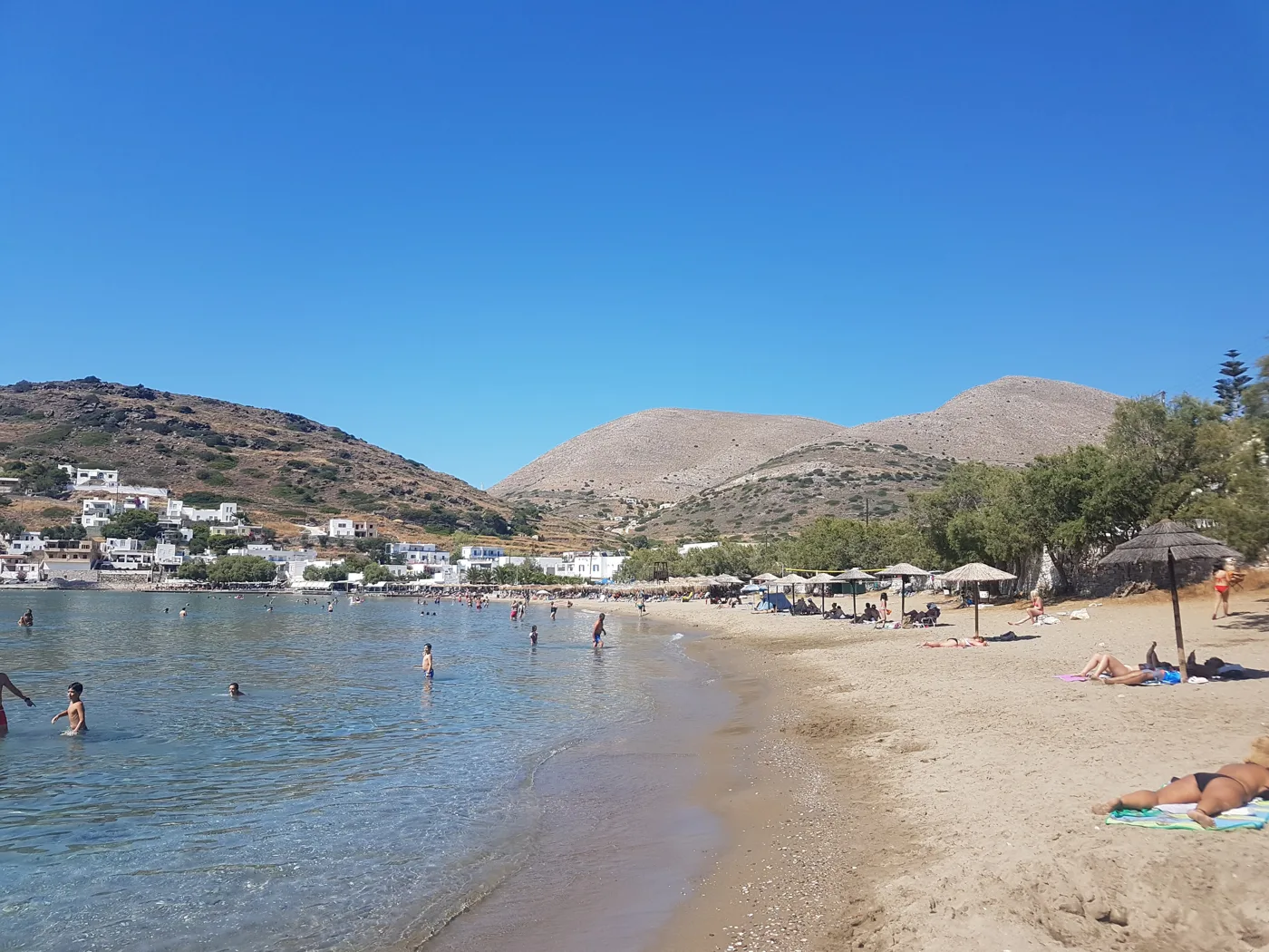 La plage de Kini avec une eau peu profonde, du monde et des parasols, des collines derrière
