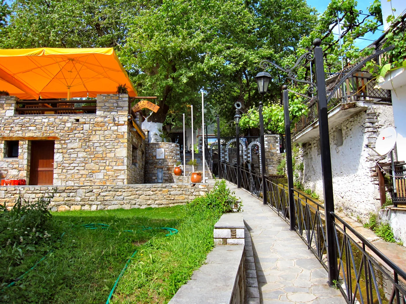 Каменна пътека в Панагия с каменни къщи, дървета и фенери