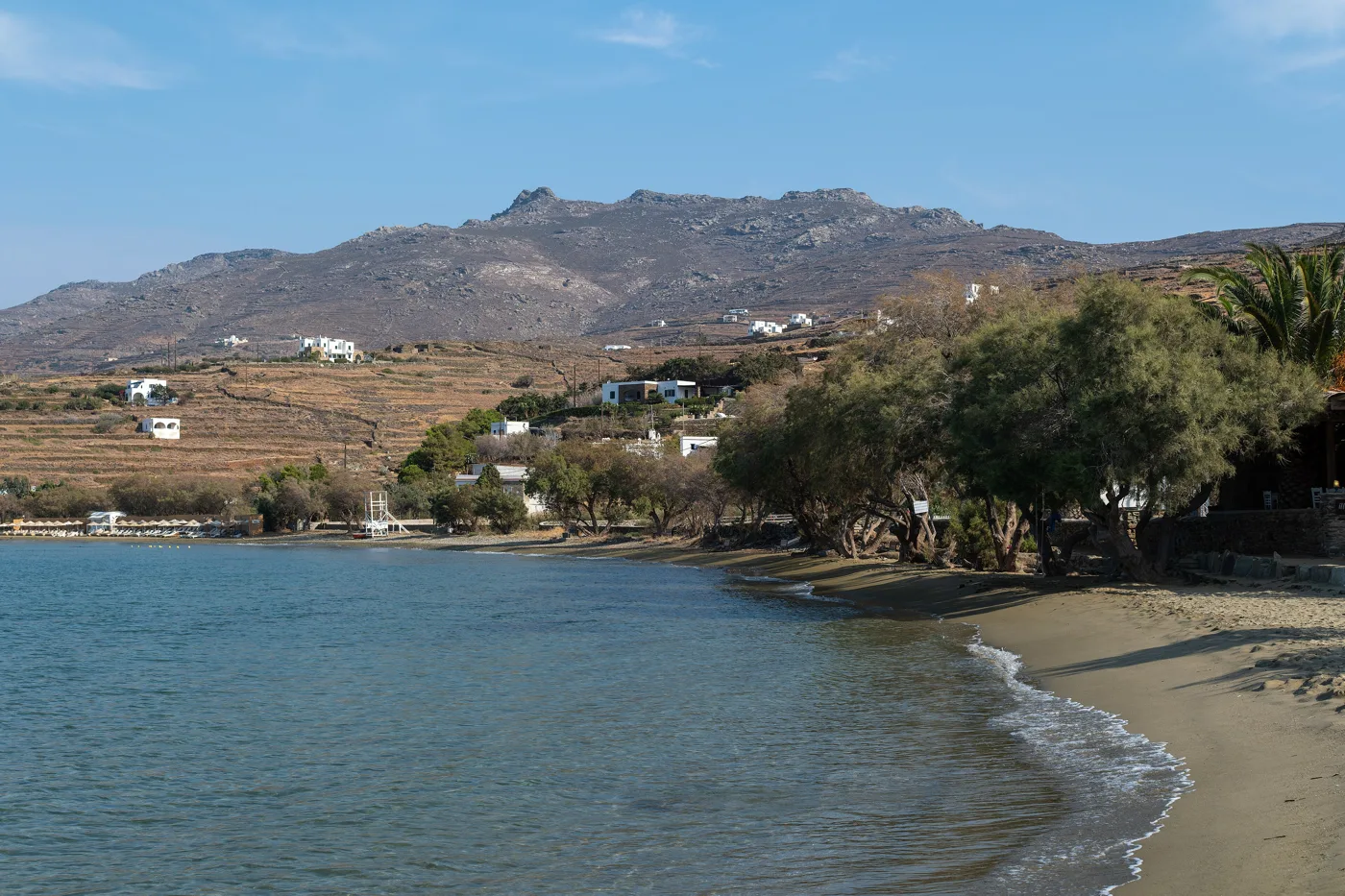 A praia de Agios Romanos com areia, tamargueiras e montanhas atrás