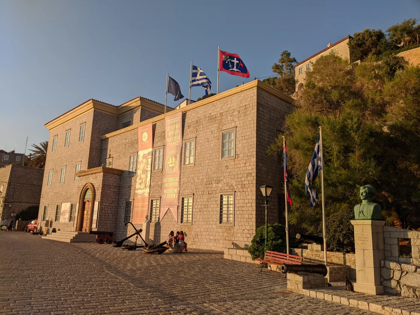 Le bâtiment en pierre des Archives historiques d’Hydra sur le port, avec des drapeaux