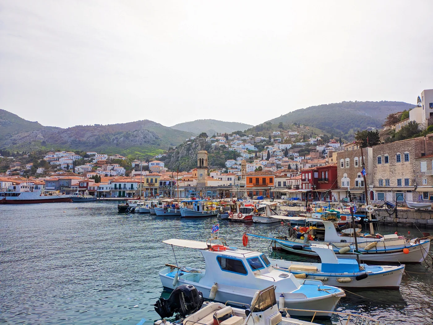 Des bateaux de pêche dans le port d’Hydra, avec des maisons en pierre et des montagnes derrière