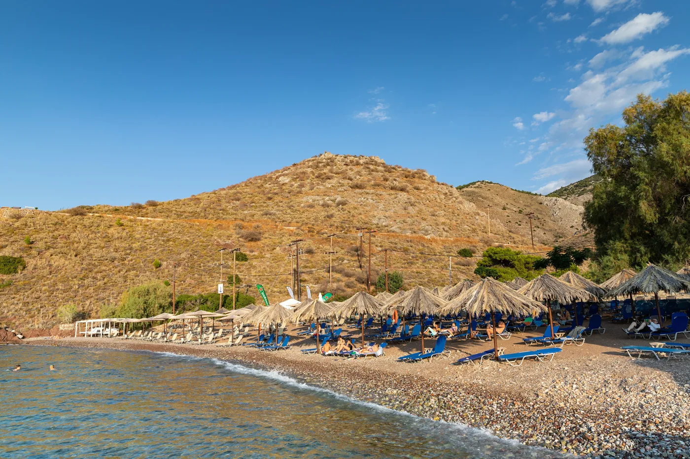La plage de Vlychos avec des galets, des parasols et une colline sèche derrière