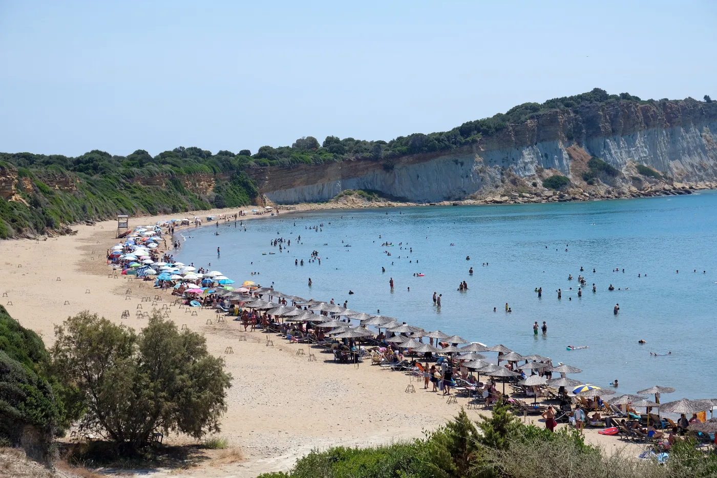 The long sandy beach of Gerakas with people, umbrellas and shallow water, below low cliffs