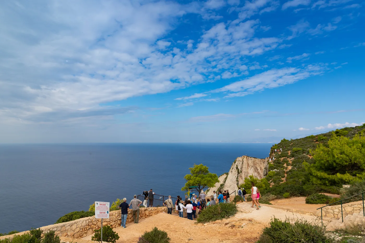 Visitors at the viewpoint above Navagio, with the sea and pine-covered hills