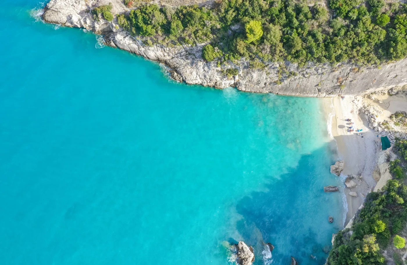 Xigia beach from above, with white pebbles and blue water below a green hill