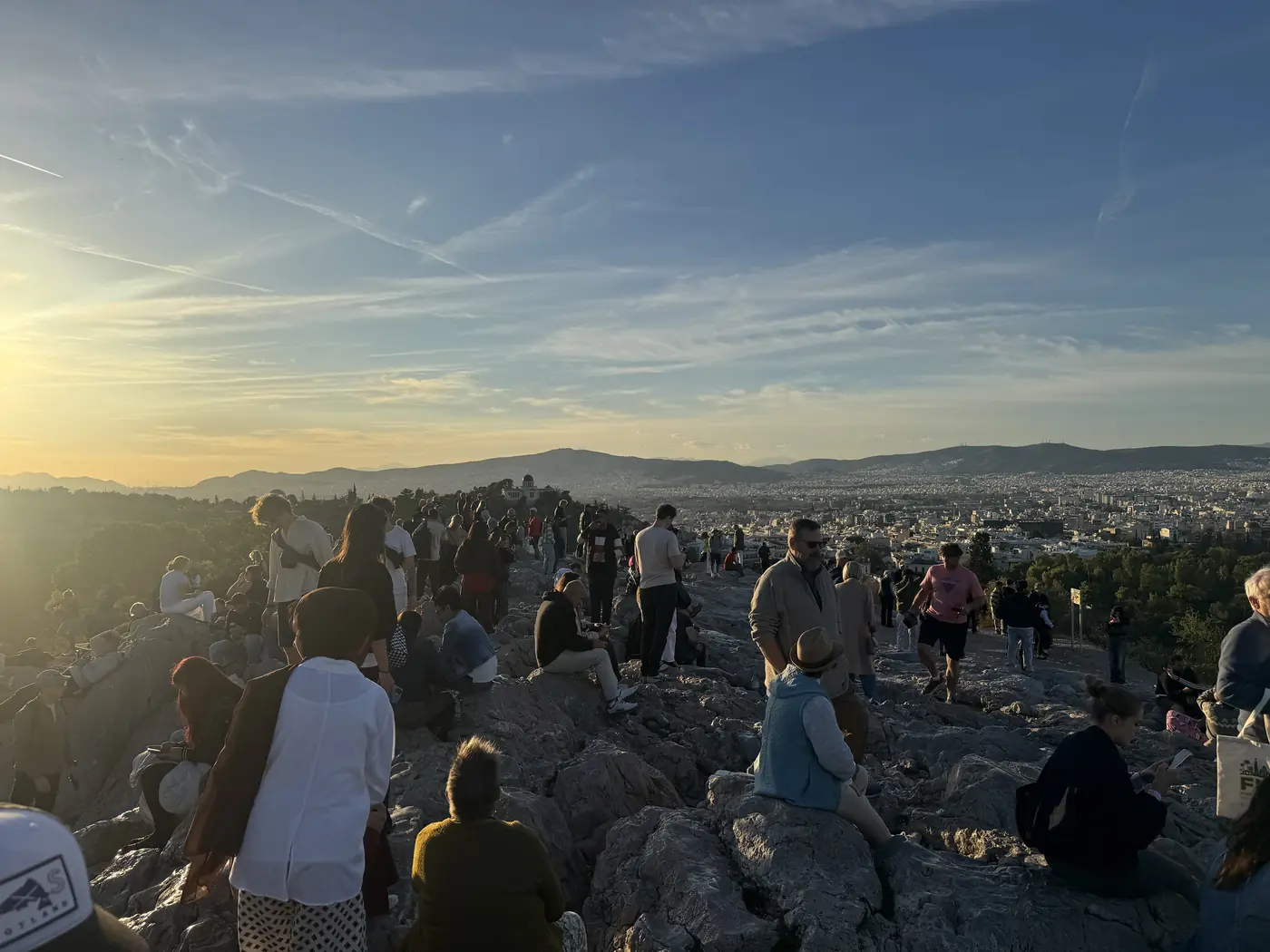 Mensen zitten bij zonsondergang op de rotsen van de Areopagus boven Athene