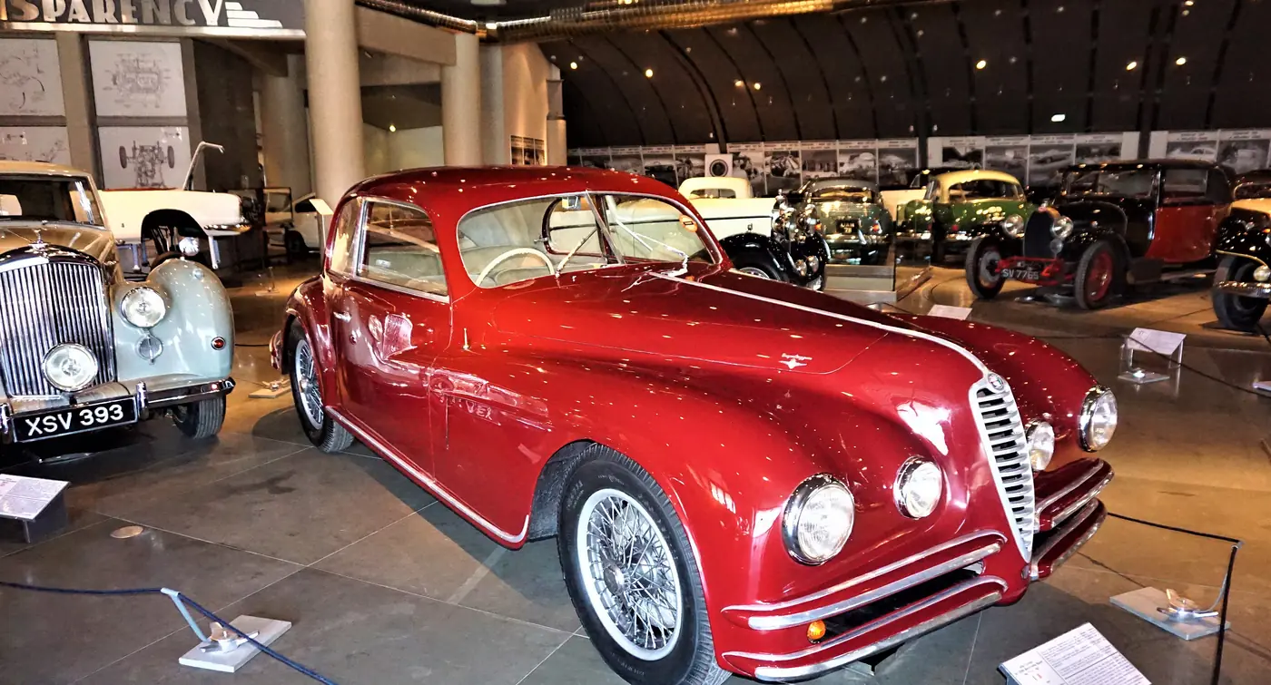 Una coupé d’epoca rossa con calandra cromata davanti a una fila di auto storiche al Museo dell’automobile