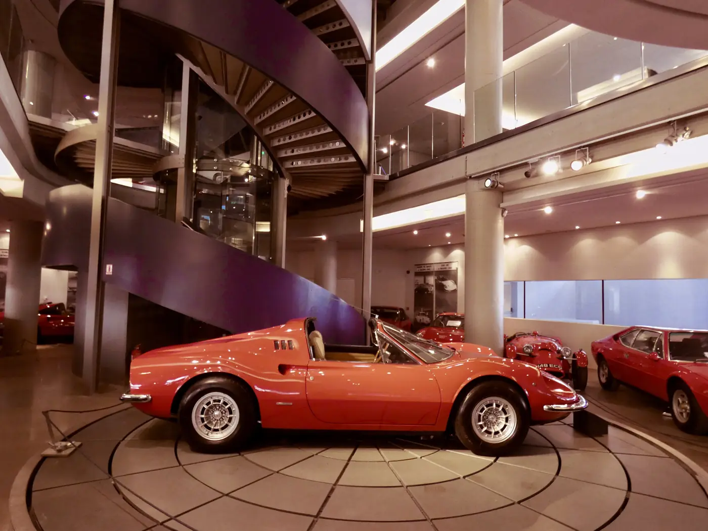 Un’auto sportiva rossa su una pedana rotonda al Museo dell’automobile, con scala e ringhiera alle spalle