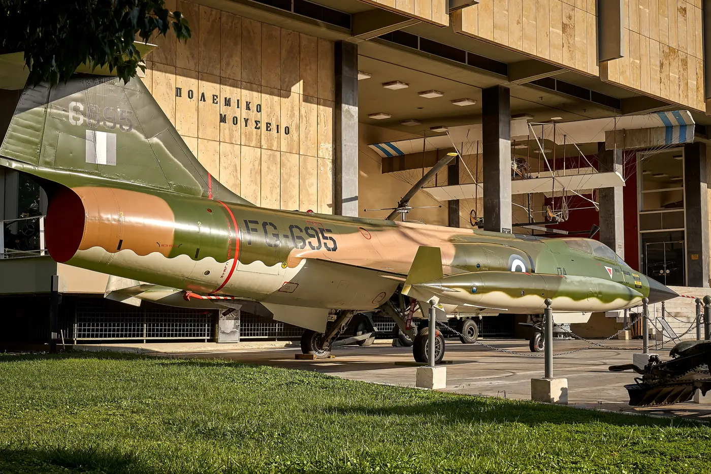 Un F-104 Starfighter verde-grigio nel cortile del Museo della Guerra di Atene, sotto l’edificio
