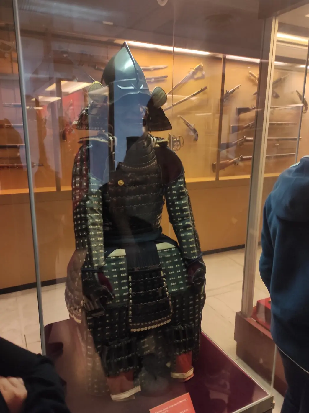 Un’armatura da samurai giapponese in una teca, con spade e pistole nelle vetrine dietro, al Museo della Guerra