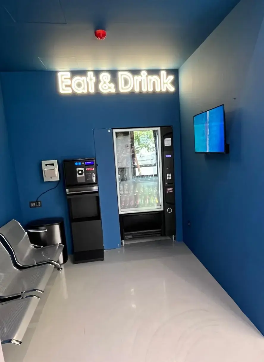 Η γωνιά Eat & Drink με τον μπλε τοίχο, τον αυτόματο πωλητή και καθίσματα αναμονής