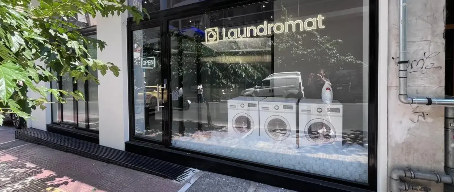 Η βιτρίνα του Laundromat στο ισόγειο της Ιουλιανού 50, με πλυντήρια ρούχων πίσω από το τζάμι