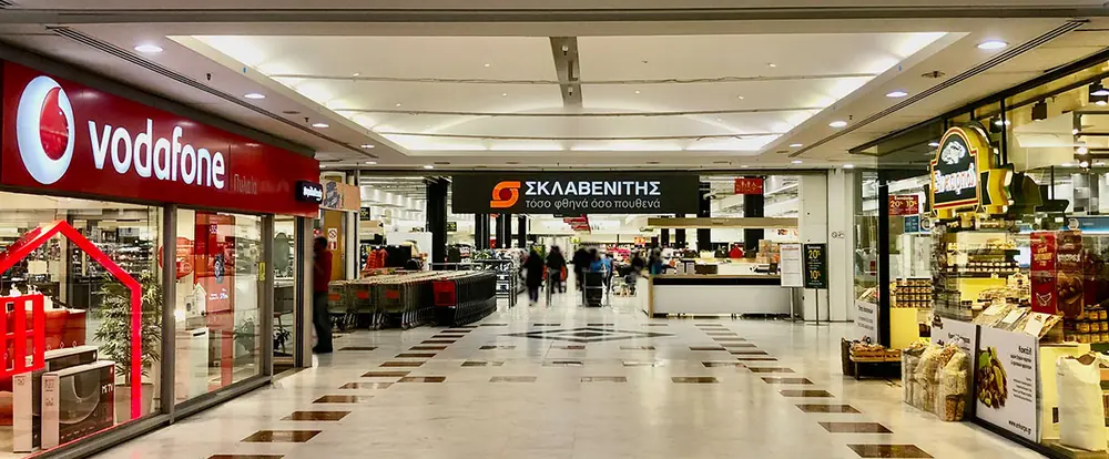 左にVodafone、前方にSklavenitisスーパーの入口があるショッピングセンターの通路